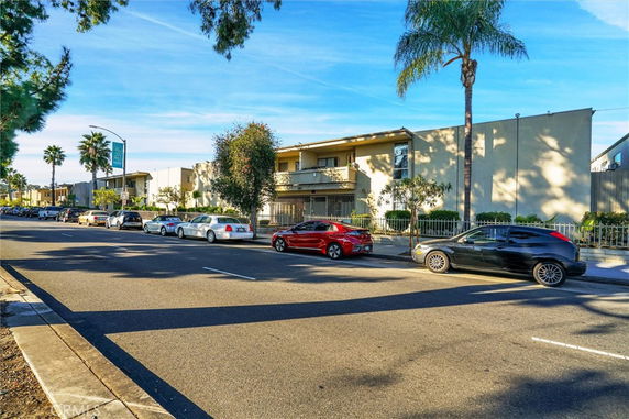 Front view of a two-story building with a balcony and parked cars in front.