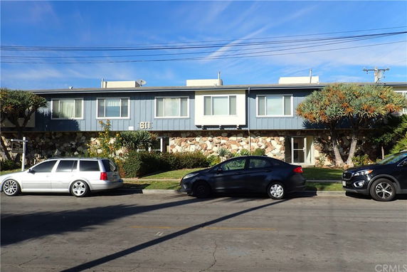 Front view of a two-story building with a stone facade and several parked cars.