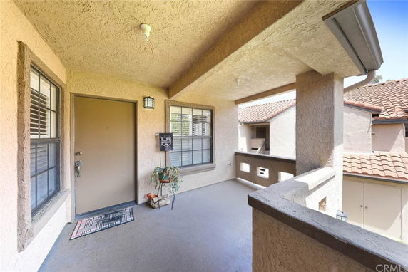 Covered outdoor entryway with door and windows, overlooking neighboring rooftops.