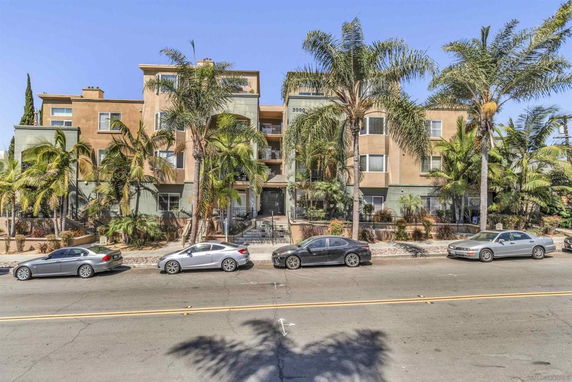 Front view of a multi-story residential building with balconies and palm trees.