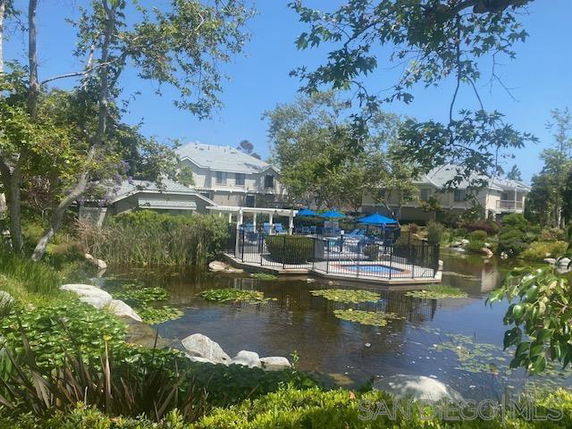 View of residential buildings surrounded by trees and a pond.