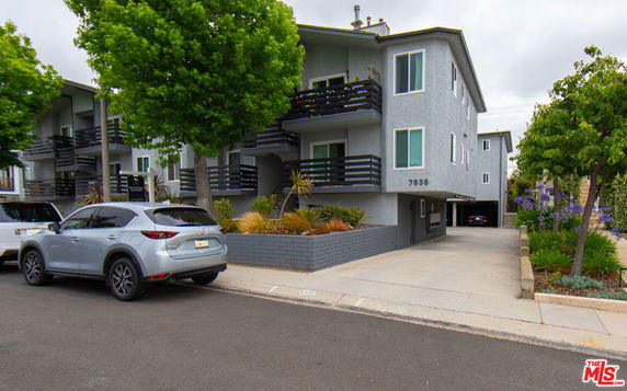 Front view of a multi-story apartment building with balconies and a driveway.