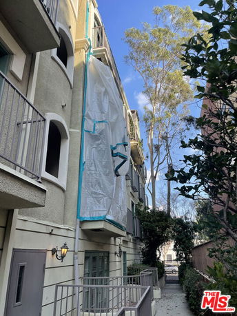 Front view of a multi-story residential building with balconies and a section covered with tarpaulin.