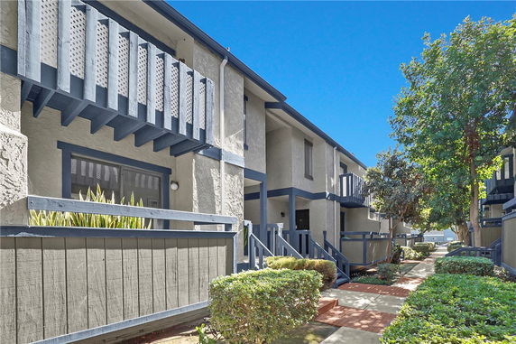 Front view of a two-story building with balconies and a walkway surrounded by greenery.