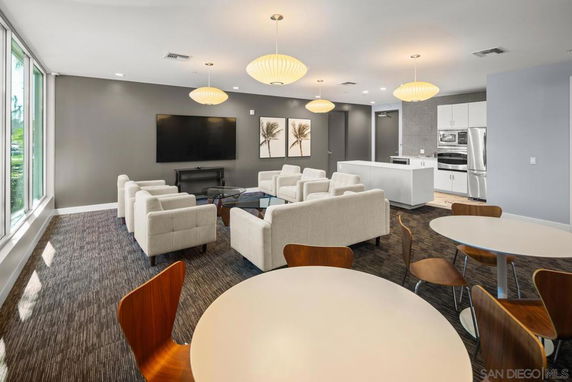 Interior view of a clubhouse with seating area, large TV, and kitchenette.