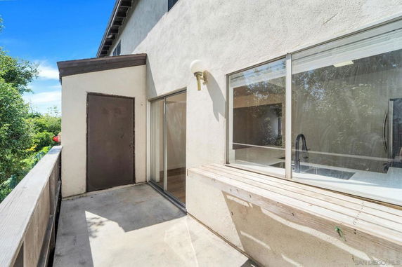 Partial view of a building exterior with a door and windows, seen from a small outdoor landing or balcony.