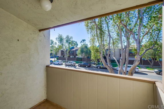 View from a balcony overlooking a street with trees and parked cars.