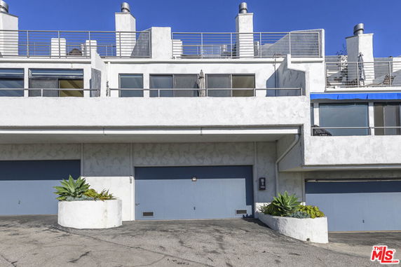 Front view of a multi-level house with garages and a rooftop terrace.