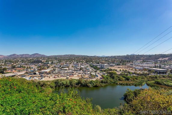 Panoramic view of a cityscape with a river and greenery in the foreground, and mountains in the background.