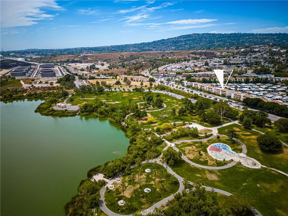 Panoramic view of a park area with a water body in the foreground and residential buildings in the distance.