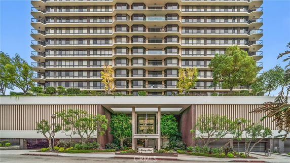 Front view of a multi-story building with balconies and landscaped entryway.