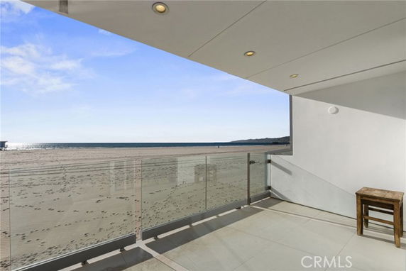 Balcony with glass railing overlooking a sandy beach and ocean view.
