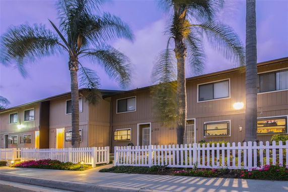 Front view of a two-story building with a picket fence and palm trees in the foreground.