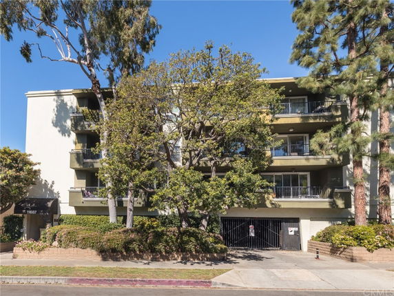 Front view of a multi-story apartment building with balconies and surrounding trees.