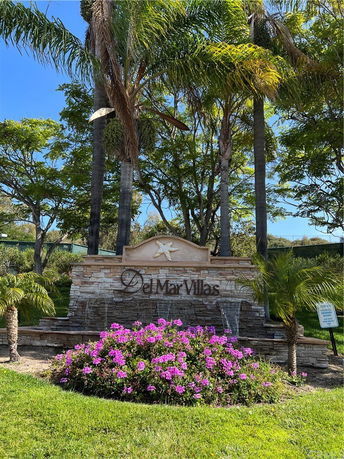 Entrance sign for Del Mar Villas surrounded by palm trees and flowering plants.