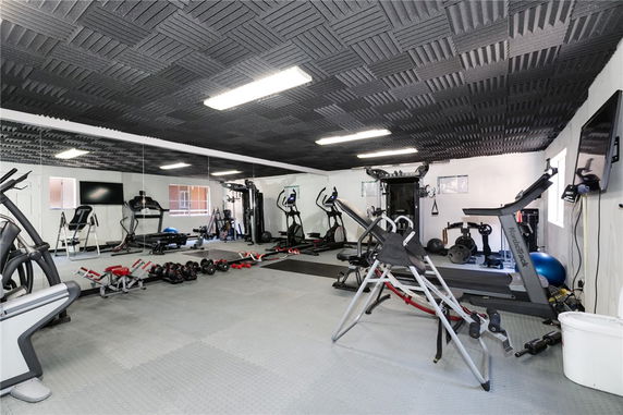 Interior of a gym area with exercise equipment and mirrored wall.