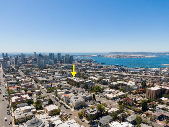 Aerial panoramic view of a coastal city with numerous buildings and skyscrapers, overlooking a body of water with boats.