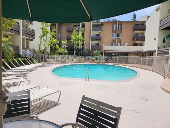 Outdoor swimming pool area with lounge chairs and apartment buildings in the background.