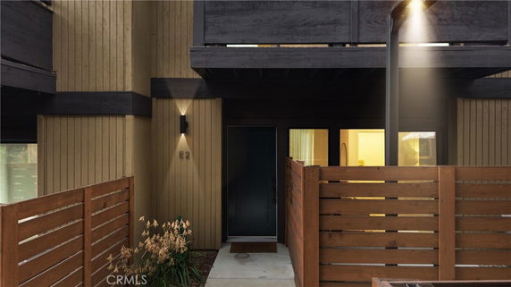 Front view of a building entrance with wood paneling and a fenced area.