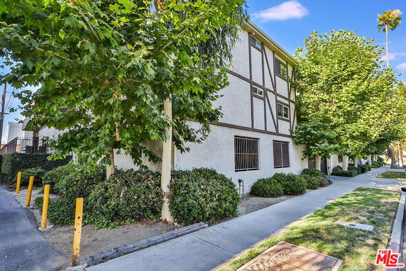 Front view of a multi-story building with Tudor-style architecture elements and trees along the sidewalk.