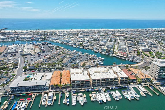 Aerial panoramic view of a coastal city with a marina and boats, residential and commercial buildings, and the ocean in the background.