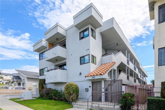 Front view of a multi-story modern building with balconies and tiled roof entrance.