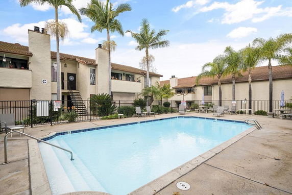 Outdoor swimming pool surrounded by multi-story buildings and palm trees.
