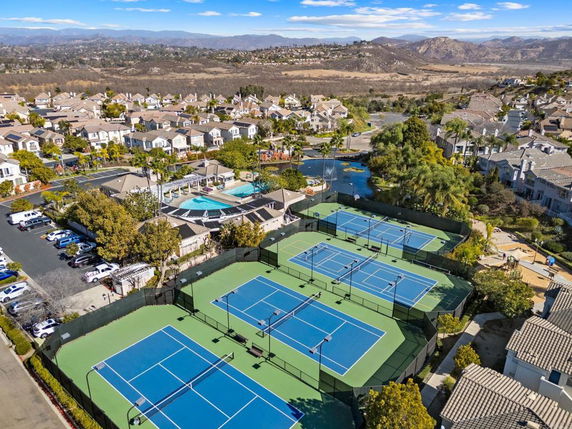 Tennis courts and swimming pool surrounded by residential buildings, with a view of distant hills.