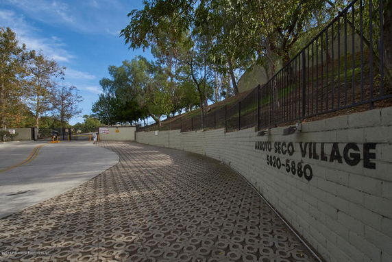 Entrance view of a gated residential area with a brick wall and driveway.