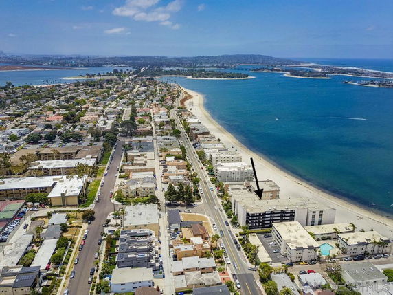 Aerial panoramic view of a coastal residential area with a road running parallel to the beachfront and buildings alongside.