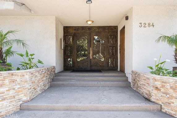Front view of a building entrance with decorative doors and stone planters.