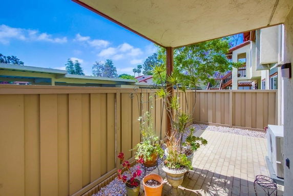 Covered patio area with fence and potted plants, adjacent to other residential structures.
