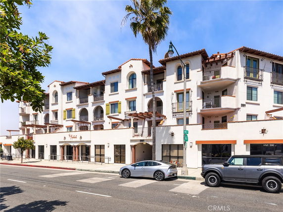 Front view of a multi-story residential building with balconies and a retail area on the ground floor.