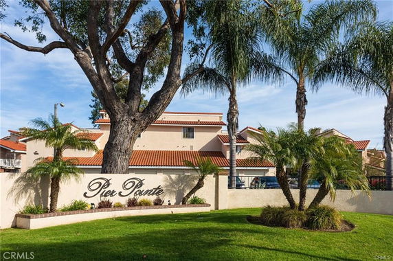 Front view of a building with red-tiled roofs behind palm trees and a sign reading 'Pier Pointe'.