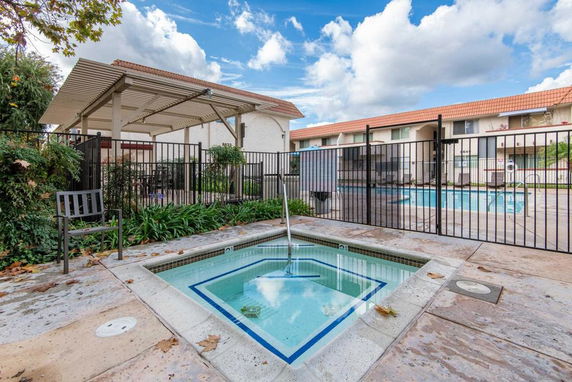 Outdoor area with a jacuzzi and swimming pool surrounded by a fence.