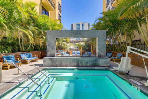 Outdoor swimming pool area with seating and tropical plants.