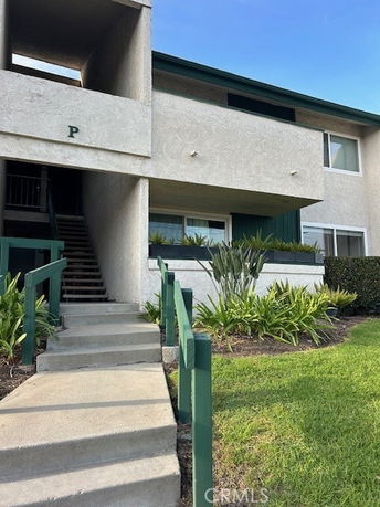 Front view of a two-story building with external stairs and a small garden area.