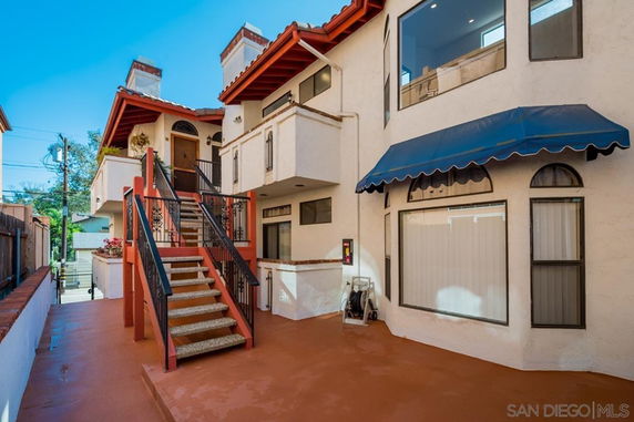 Front view of a multi-story house with an external staircase and blue awning.