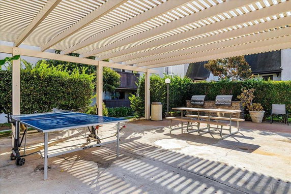 Outdoor recreational area with a ping pong table and barbecue grills under a pergola.