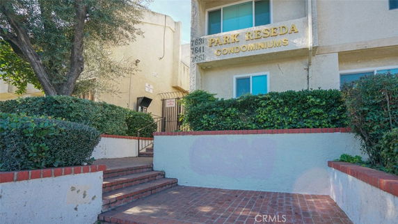 Front view of a multi-story condominium building with brick stairs and hedges.