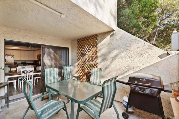Outdoor patio area with a glass table, chairs, and a barbecue grill.