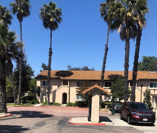 Front view of a two-story building with palm trees in a parking area.