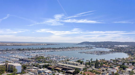 Panoramic view of a marina with boats and buildings, overlooking a body of water and hills in the distance.