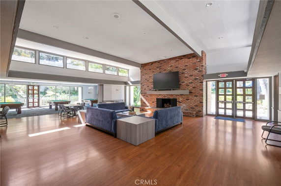 Spacious room with large windows, seating area, pool tables, and a brick fireplace.