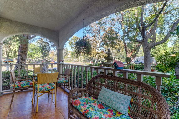 View from a covered porch with wicker and cushioned seating, looking out onto a garden area with mature trees.