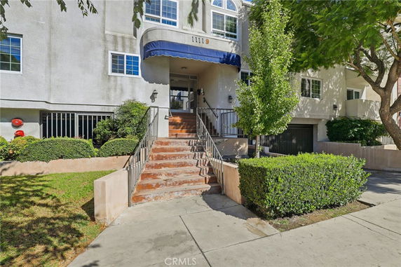 Front view of a multi-story building with stairs leading to the entrance and a blue awning.
