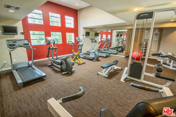 Indoor gym area with exercise equipment, including treadmills and weights.