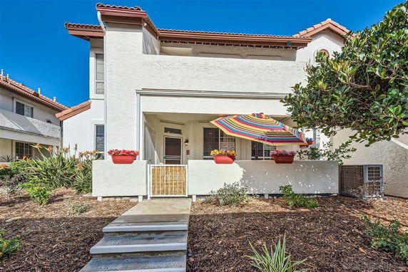 Front view of a multi-story house with a balcony and colorful umbrella.