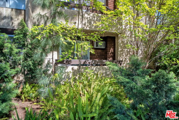Front view of a multi-story residential building with a balcony and surrounded by lush greenery.