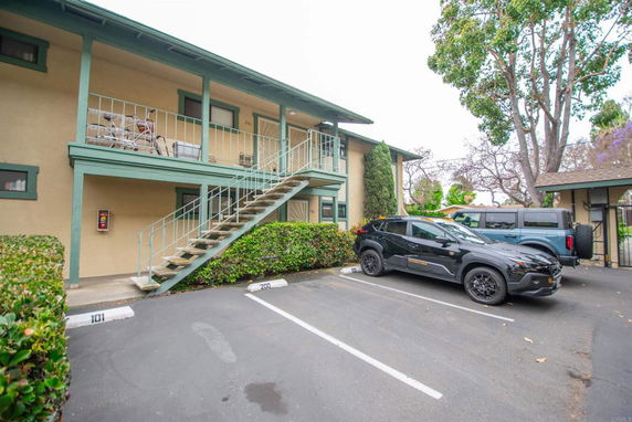 View of parking area in front of a two-story building with staircase.